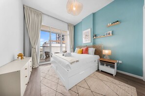 A modern bedroom with a large bed, a nightstand, a desk, and a view of the outside. - Stayshort - Comfortable 1BR Apartment in JVT With Gym Pool Sleeps 2 (Dubai)
