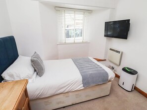 Ein Schlafzimmer mit einem Bett, einem Fenster, einem an der Wand befestigten Fernseher, einem Heizkörper und einem Papierkorb.