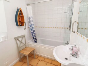 Ein Badezimmer mit einer Badewanne, einer Dusche, einem Waschbecken, einem Holzstuhl und einem Regal mit Dekoration.