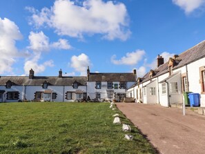 Eine Reihe traditioneller weißer Gebäude mit einer Grünfläche davor, einem klaren Himmel und einem gepflasterten Weg.