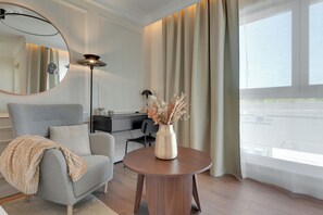 A modern living room with a grey sofa, a round wooden coffee table, a floor lamp, and a large window with curtains. - Perspektywa Apartment with balcony (Gdańsk)