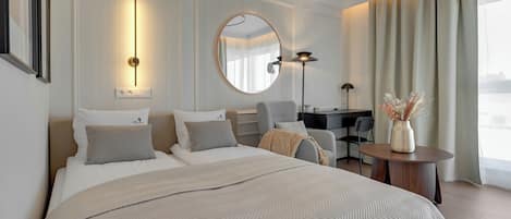 A modern hotel room with a large bed, a round mirror, a desk, and a view of the city.
