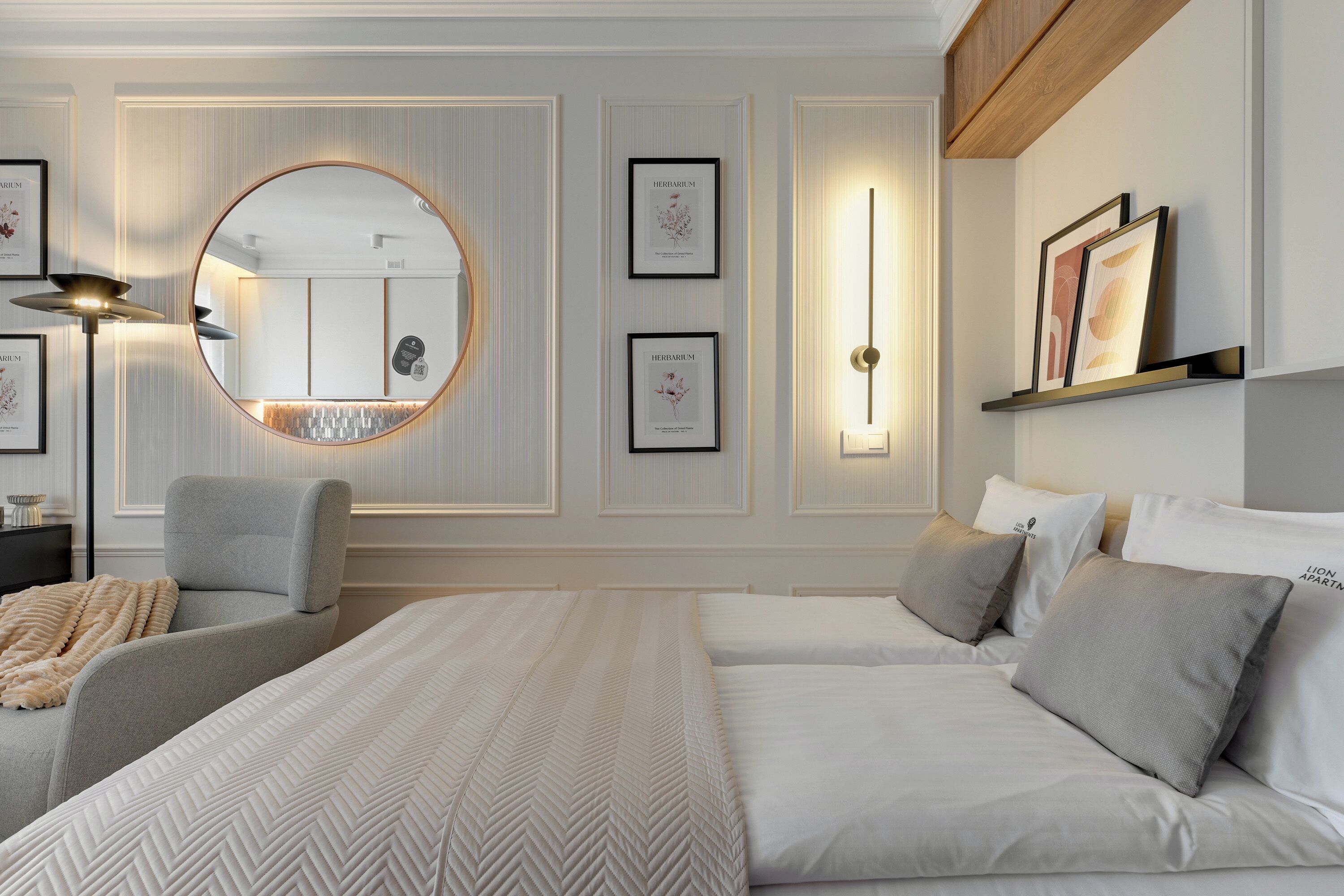Un dormitorio moderno con una cama grande, un espejo redondo e impresiones botánicas enmarcadas en la pared.