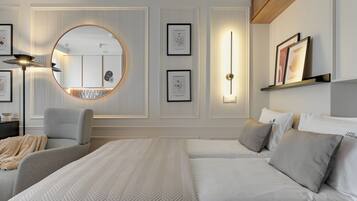 A modern bedroom with a large bed, a round mirror, and framed botanical prints on the wall.