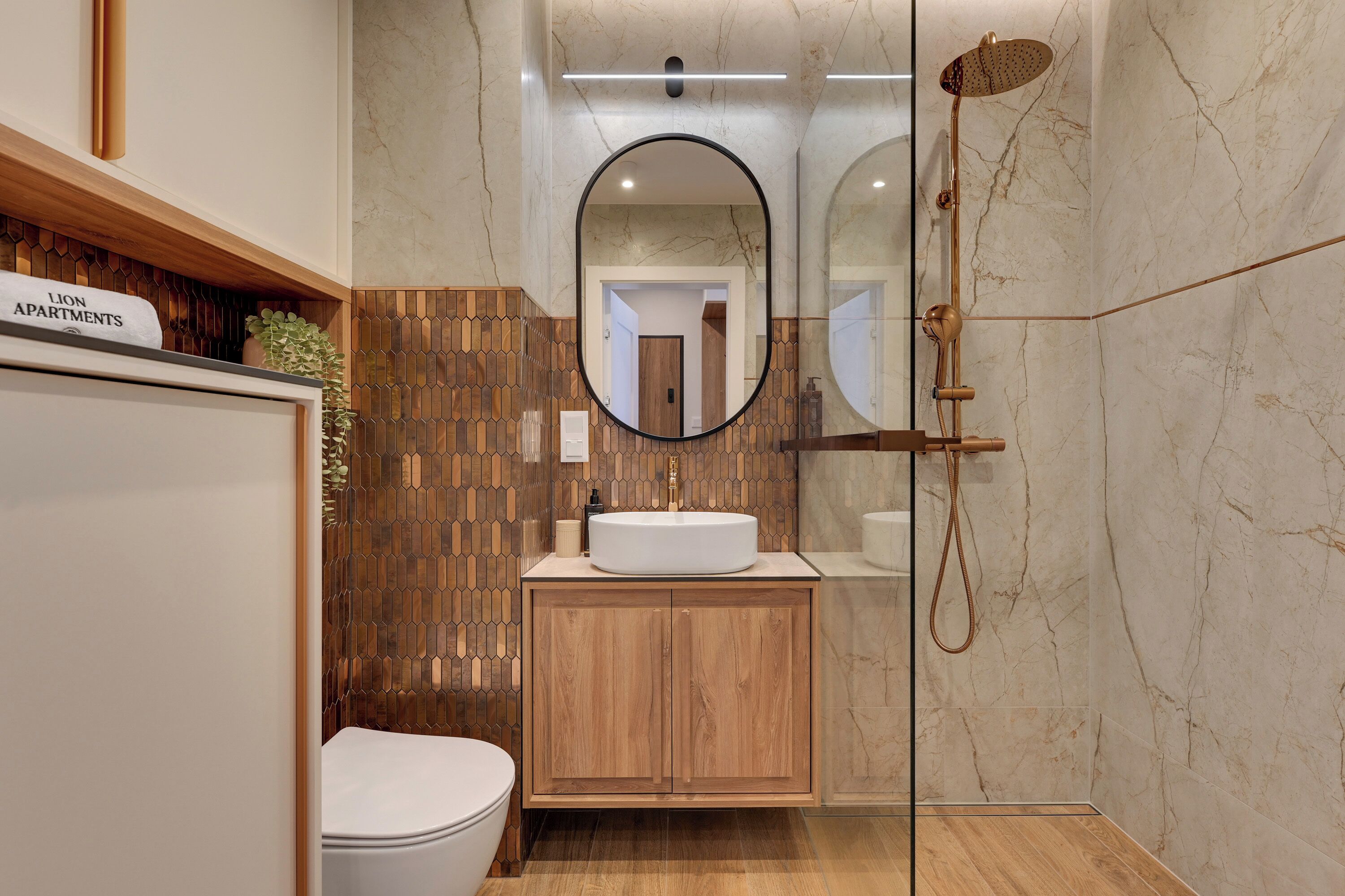 A modern bathroom with a wooden vanity, a round mirror, a glass-enclosed shower, and a marble-tiled wall.