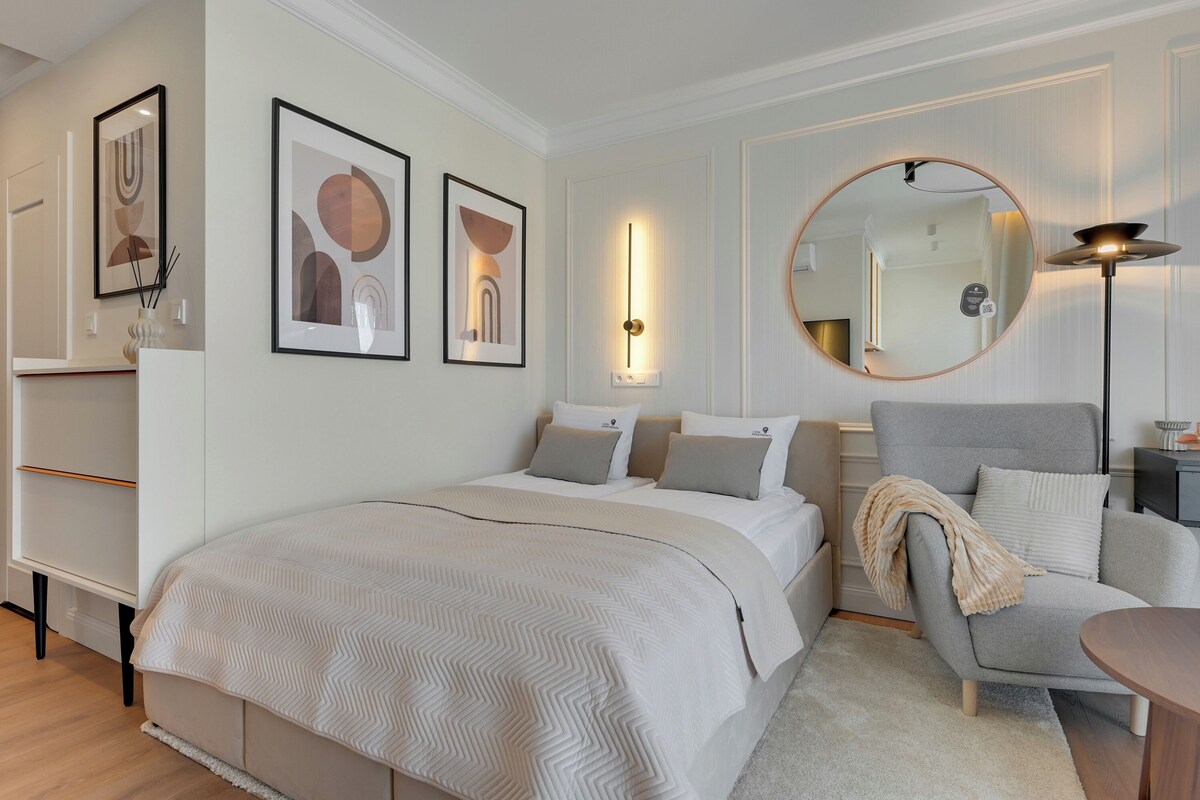 A bedroom with a bed, a chair, a round mirror, and wall-mounted artwork.