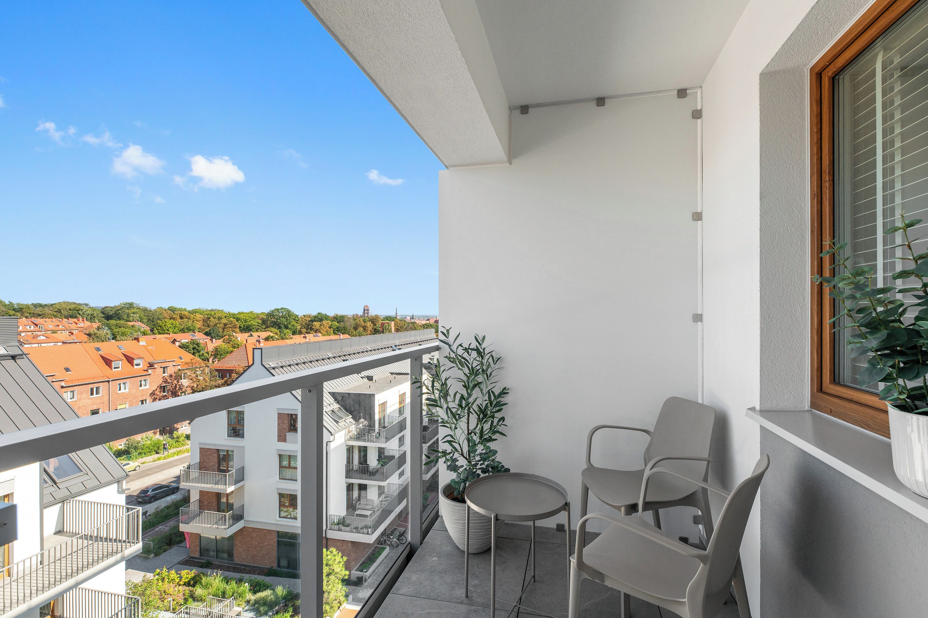 En balkong med utsikt över ett bostadsområde, en krukväxt och två stolar.
