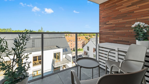 Ein Balkon mit Blick auf Gebäude, einem Tisch, Stühlen und Kübelpflanzen.