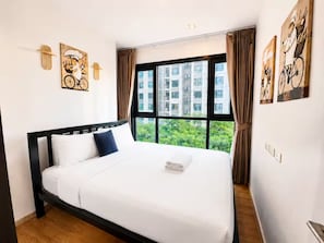 Hotellihuone, jossa on suuri sänky, ikkunasta avautuva näkymä vehreään maisemaan ja taideteoksia seinillä.