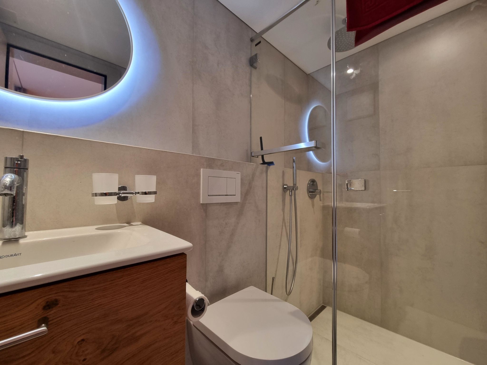 Ein modernes Badezimmer mit einer Duschkabine aus Glas, einer weißen Toilette und einem hölzernen Waschtisch mit weißem Waschbecken.
