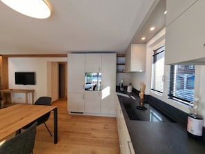 A modern kitchen with white cabinets, a black countertop, and a wooden dining table. - Haus Rio Appartement/Fewo Appartement/Fewo by Interhome (Saas-Fee)