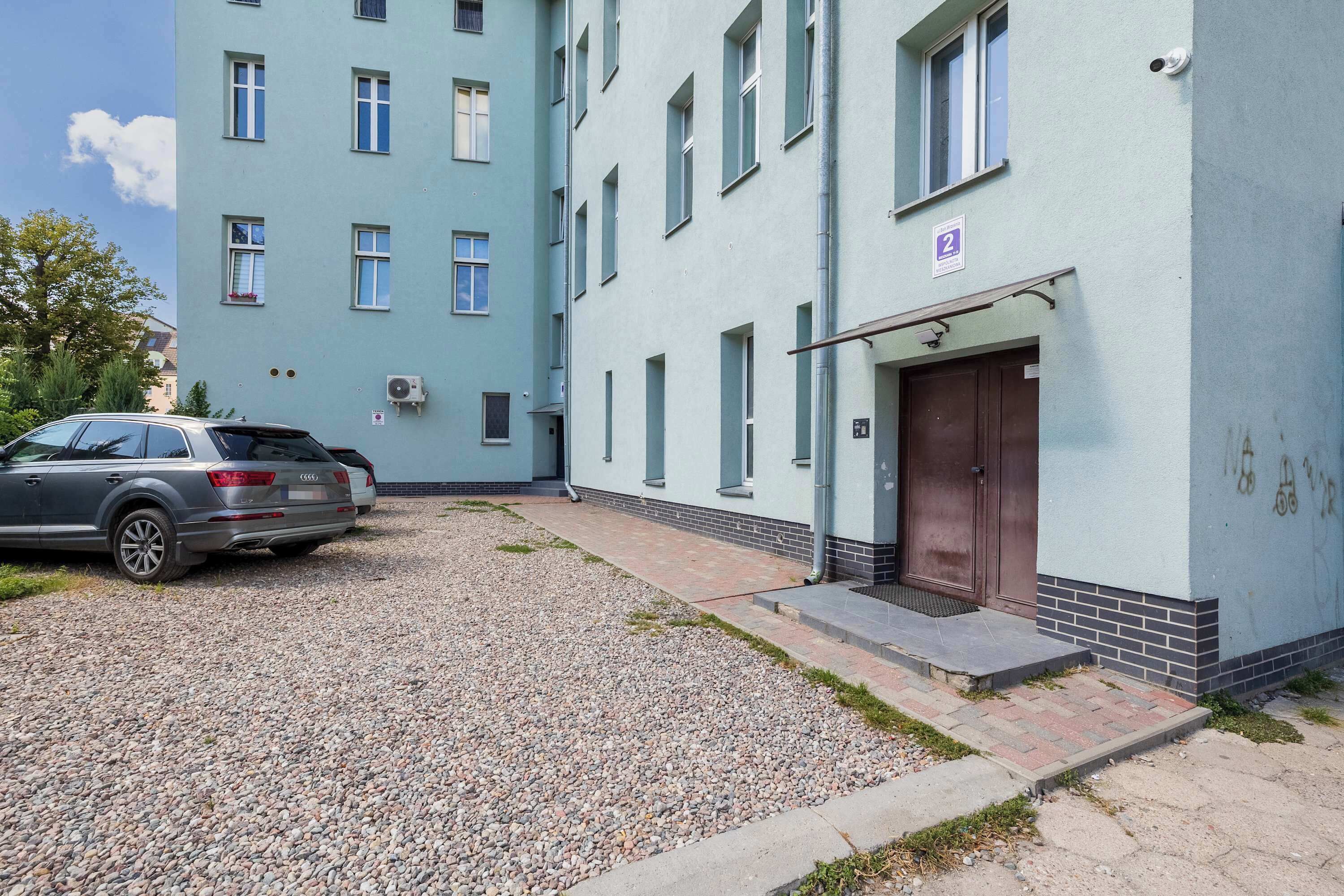 Ein Gebäude mit mehreren Fenstern und einer Tür, eine Schotterauffahrt und ein geparktes Auto.