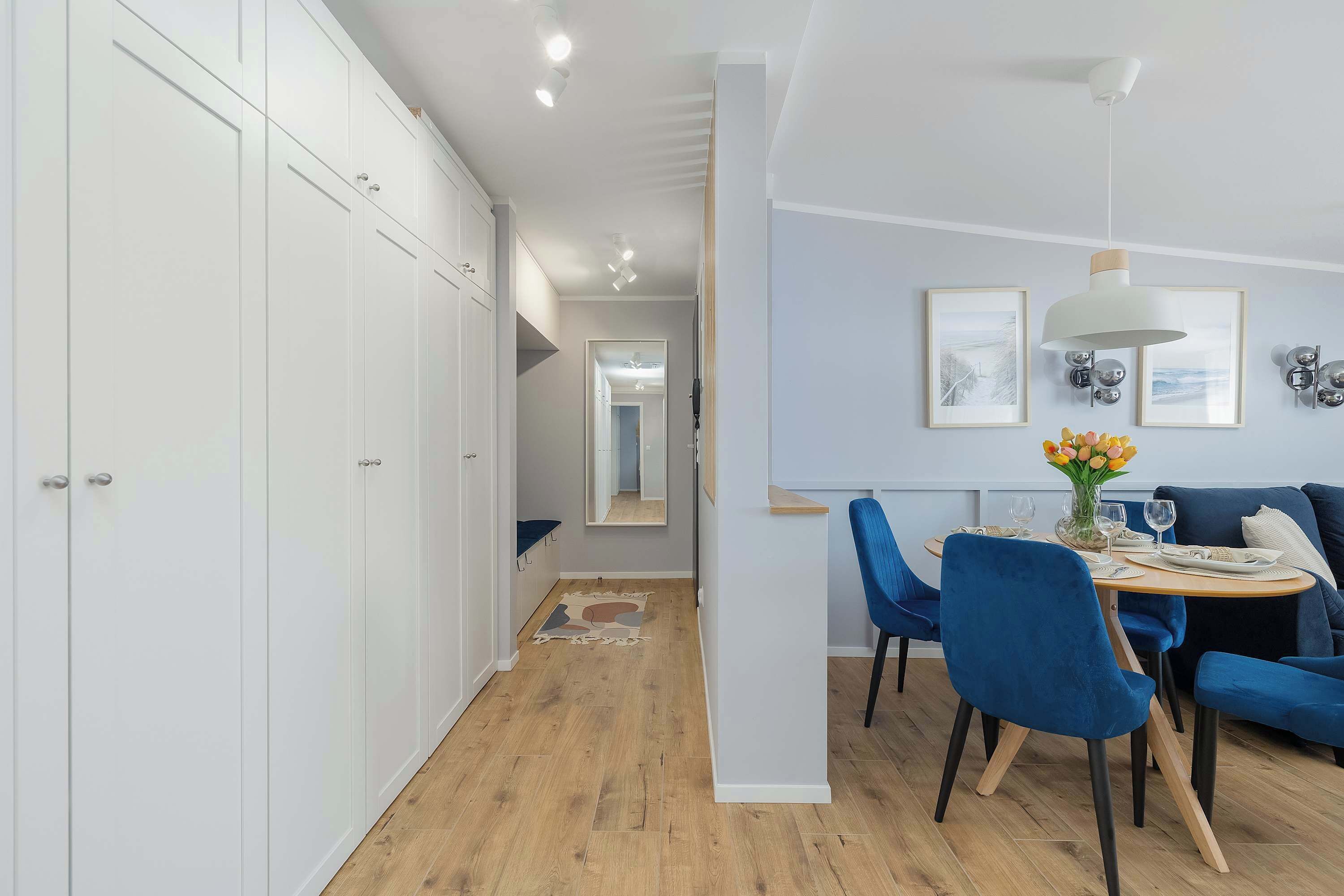 A modern interior with a dining area, blue chairs, a table with a vase of flowers, and a white wardrobe.