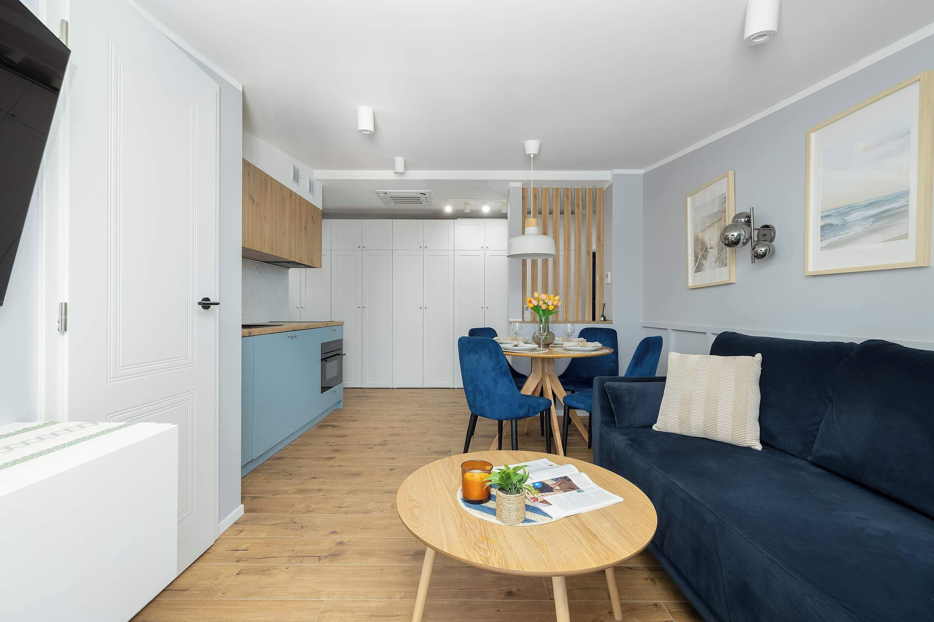 Ein modernes Wohnzimmer mit einem blauen Sofa, einem runden Holztisch und einem Essbereich mit blauen Stühlen.
