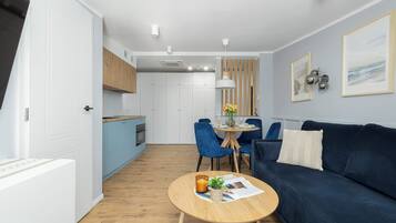 Ein modernes Wohnzimmer mit einem blauen Sofa, einem runden Holztisch und einem Essbereich mit blauen Stühlen.