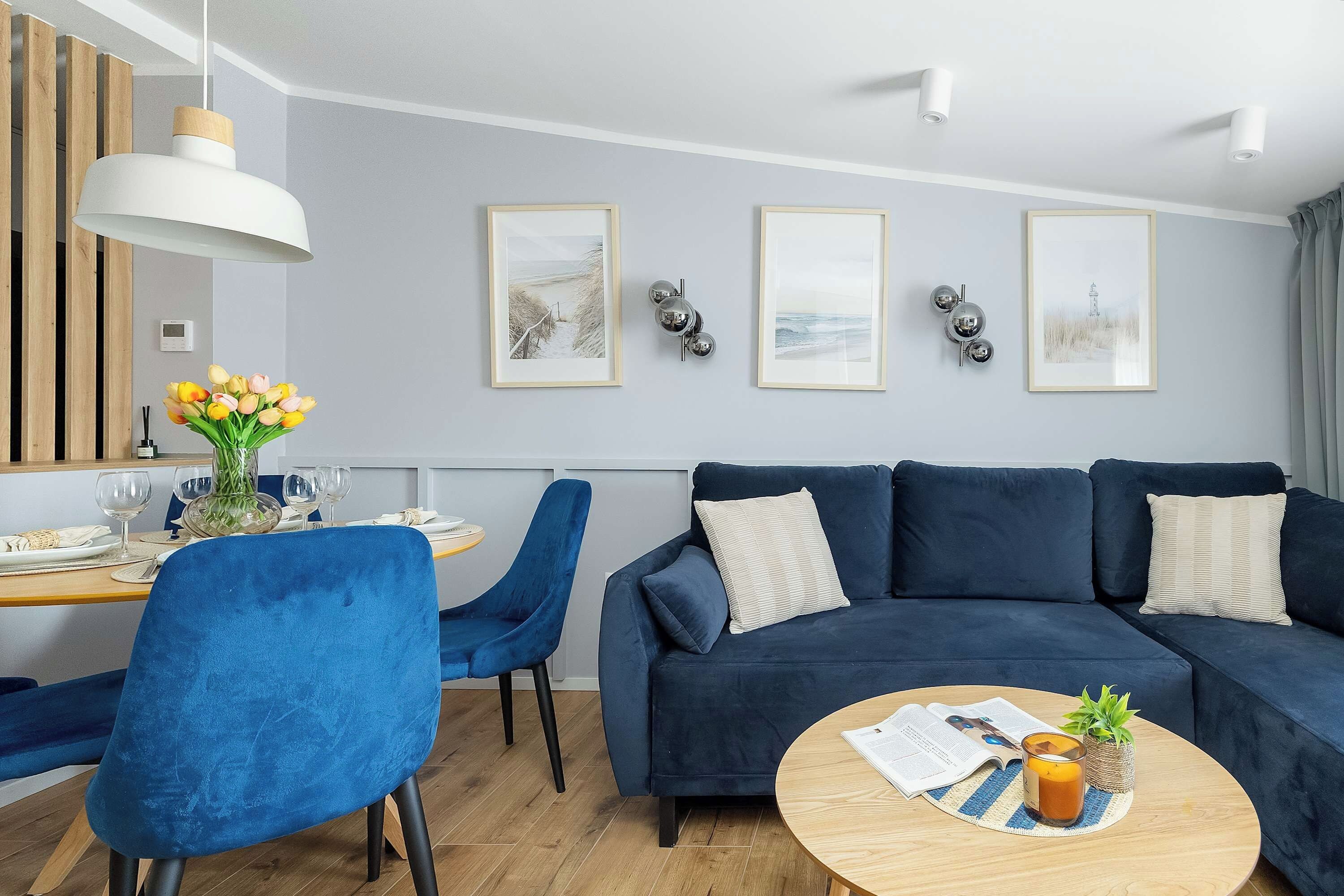 A modern living room with a blue sofa, a dining table with chairs, and artwork on the wall.