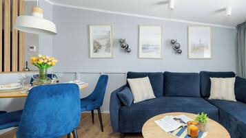Ein modernes Wohnzimmer mit einem blauen Sofa, einem Esstisch mit Stühlen und Kunstwerken an der Wand.