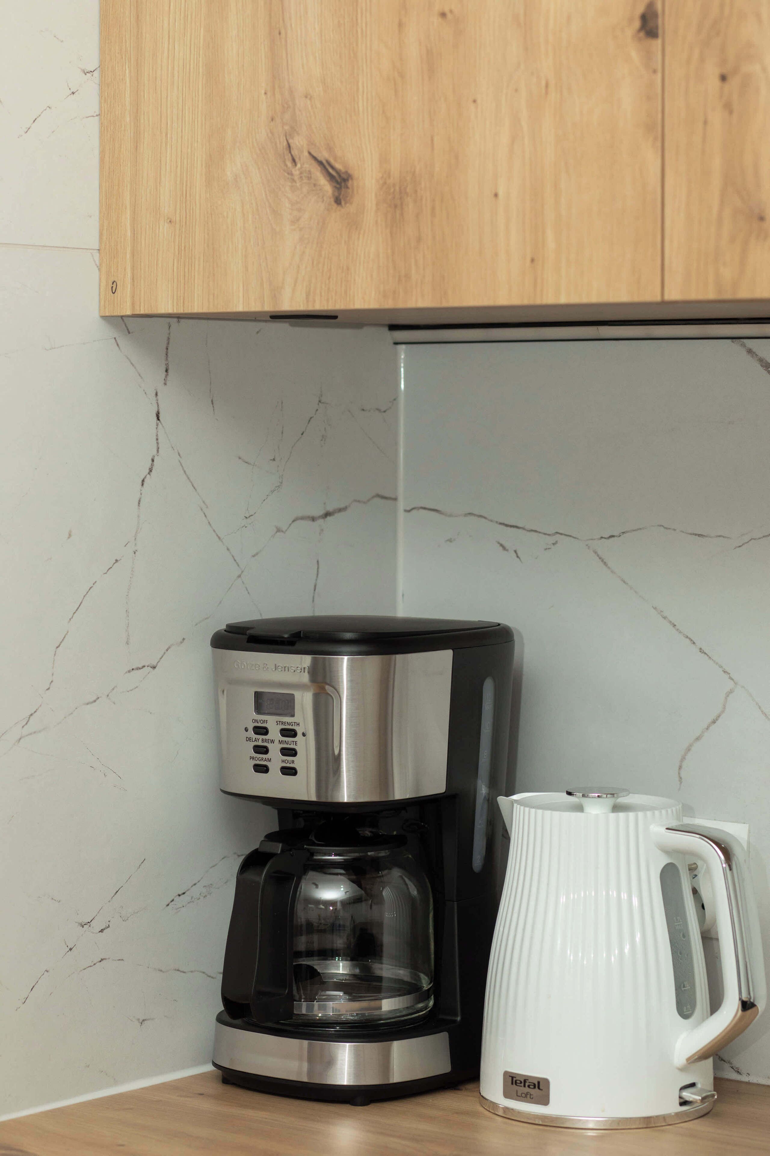 Eine Kaffeemaschine mit digitaler Anzeige und einer weißen Kaffeekanne auf einer Küchenarbeitsplatte.