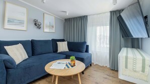 Una sala de estar con un sofá azul, una mesa de centro de madera con una planta y un televisor montado en la pared.