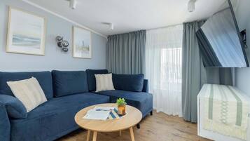 Ein Wohnzimmer mit einem blauen Sofa, einem Holztisch mit Pflanze und einem an der Wand befestigten Fernseher.