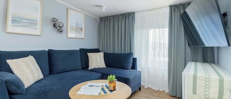 Una sala de estar con un sofá azul, una mesa de centro de madera con una planta y un televisor montado en la pared.