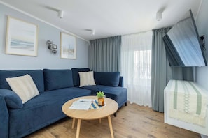 Ein Wohnzimmer mit einem blauen Sofa, einem Holztisch mit Pflanze und einem an der Wand befestigten Fernseher.