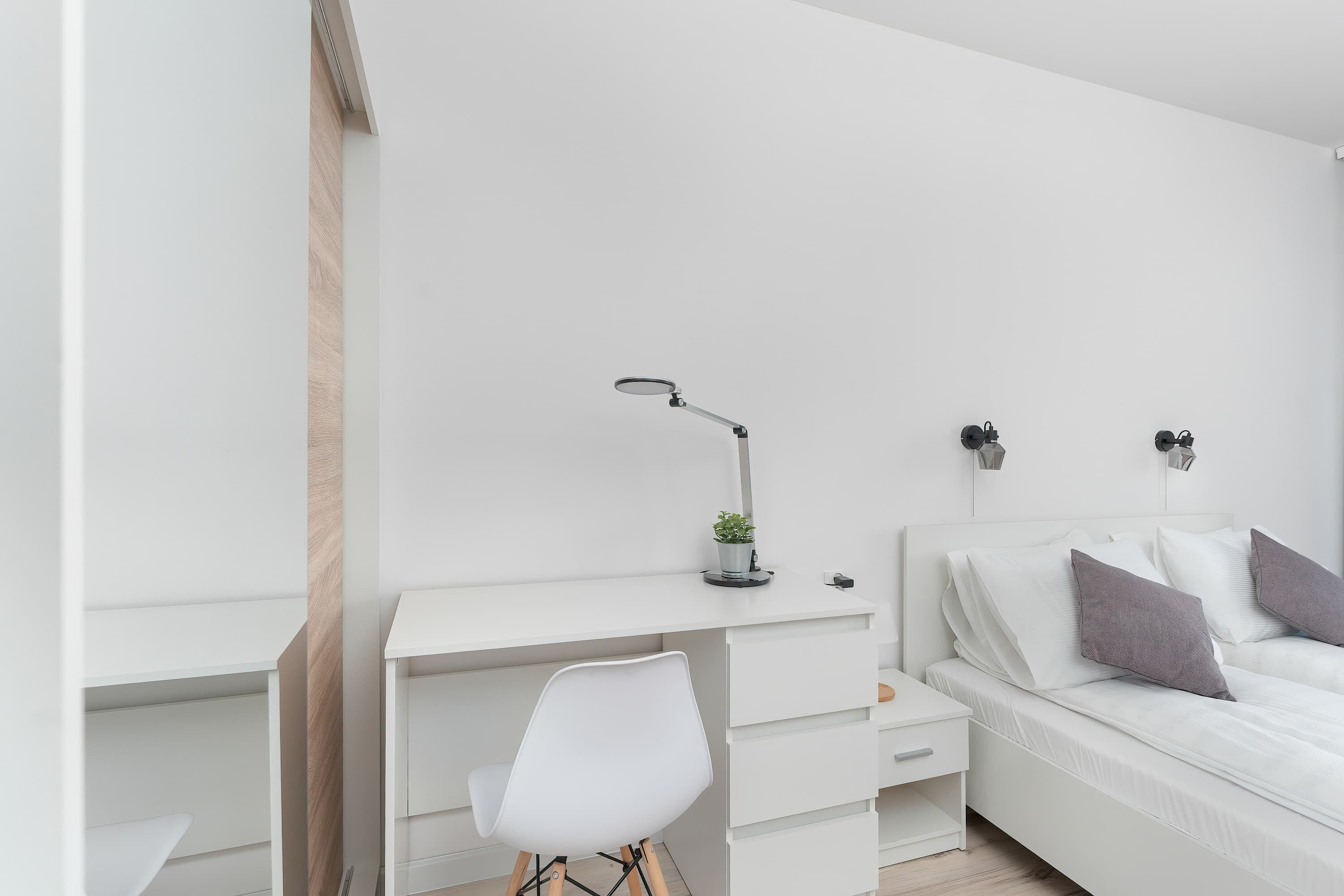 A minimalist bedroom with a white desk, chair, and bed.
