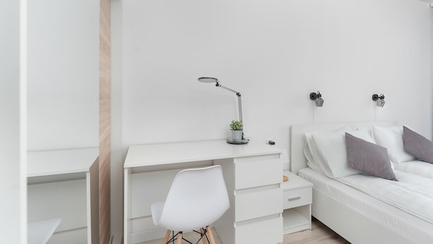 Un dormitorio minimalista con un escritorio blanco, una silla y una cama.