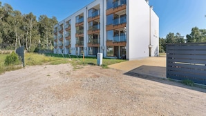 Un edificio residencial moderno de varios pisos con balcones, entrada protegida y camino de acceso de grava.