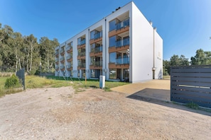 A modern multi-story residential building with balconies, a gated entrance, and a gravel driveway. - Air Conditioned Apartment with Balcony | Parking (Mielno)