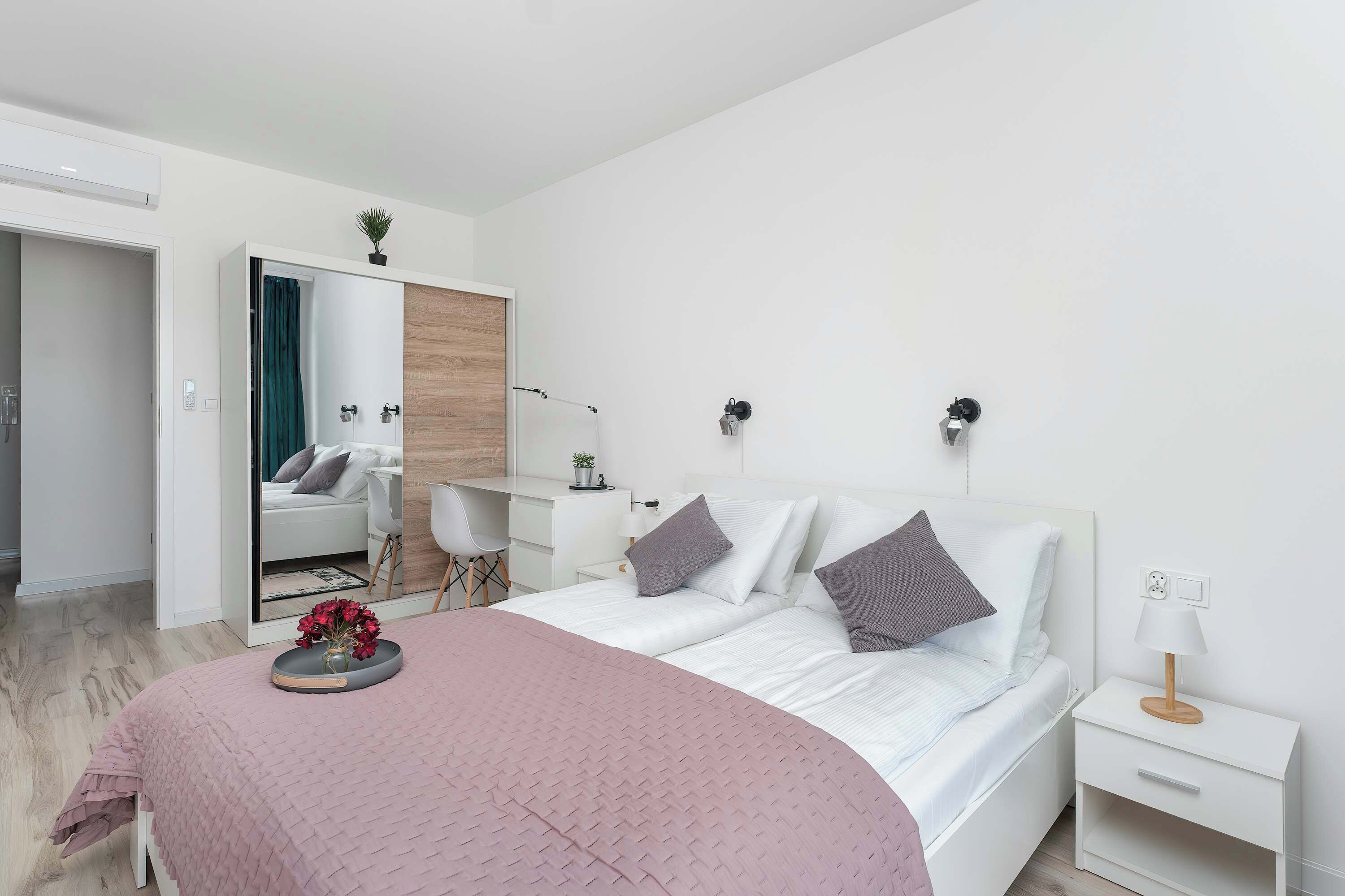 Een moderne slaapkamer met een bed, nachtkastjes, een bureau en een spiegel.
