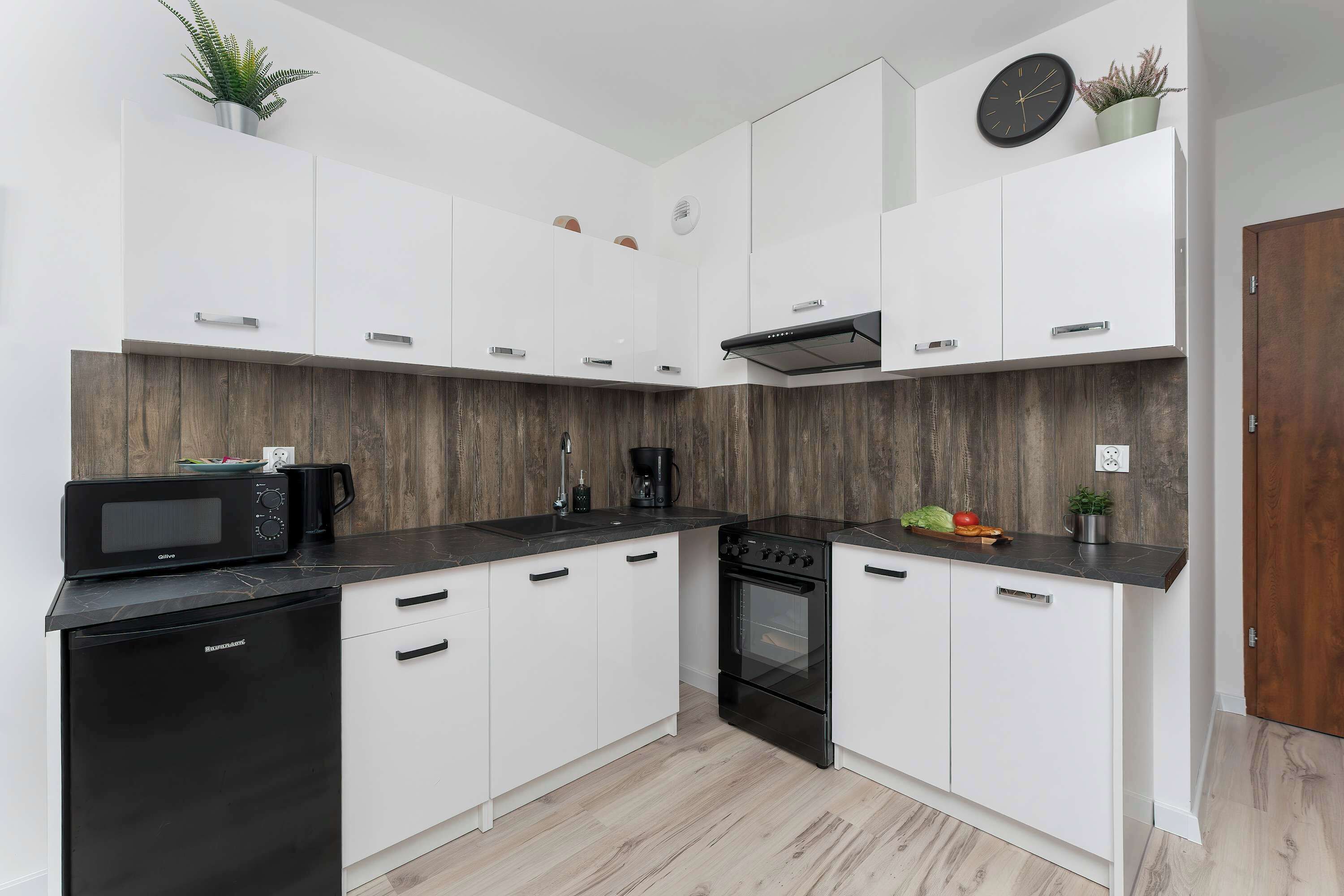 Een moderne keuken met witte kasten, een zwarte magnetron, een fornuis en een spoelbak.