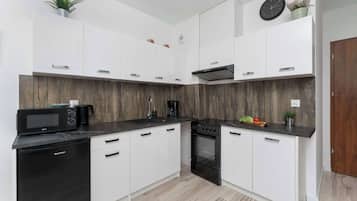 Een moderne keuken met witte kasten, een zwarte magnetron, een fornuis en een spoelbak.