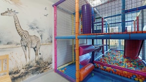 Un área de juegos con piscina de pelotas, toboganes y un mural de una jirafa.