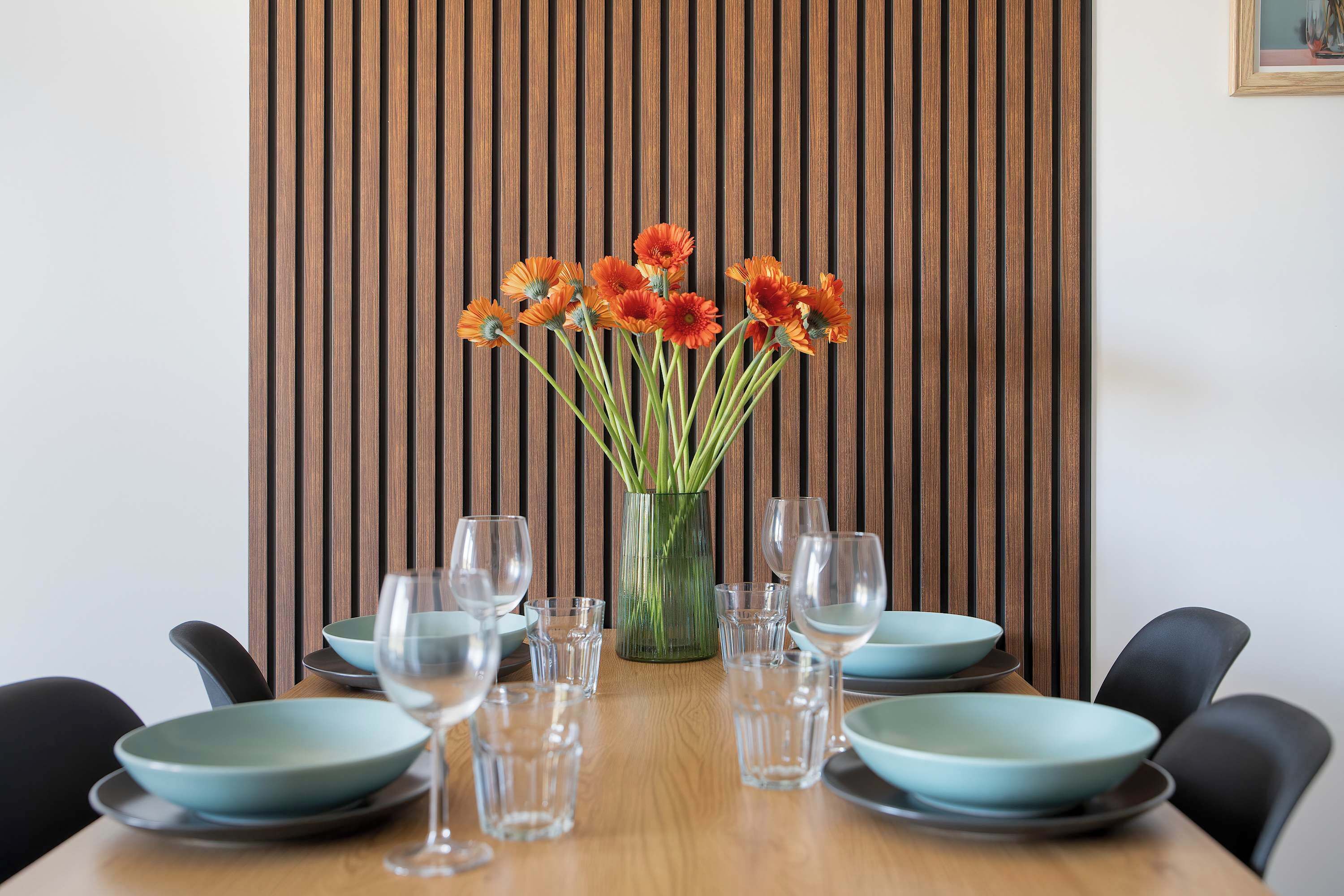 Uma mesa de jantar com um vaso de flores laranjas, copos de vidro transparentes e pratos azuis.