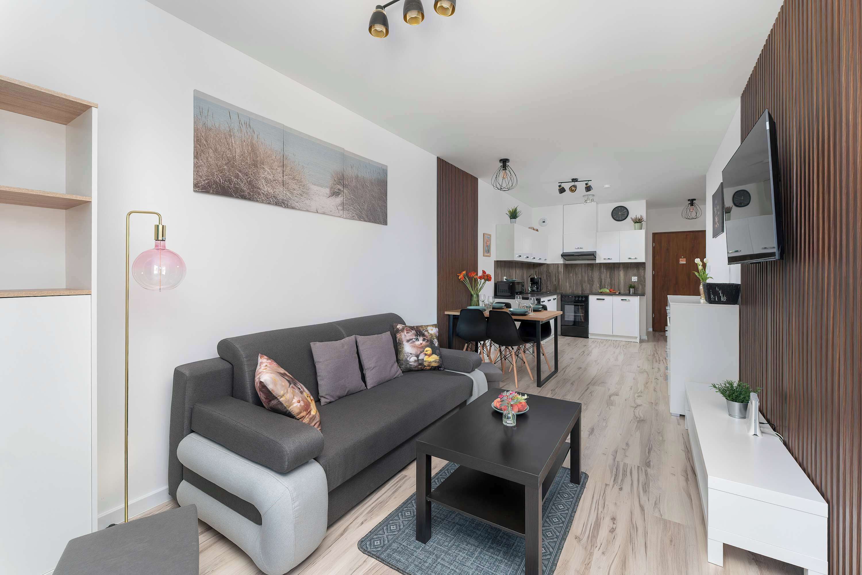 Een moderne woonkamer met een grijze bank, een salontafel en een eethoek, met een keuken op de achtergrond.