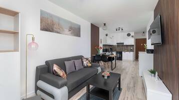 Een moderne woonkamer met een grijze bank, een salontafel en een eethoek, met een keuken op de achtergrond.