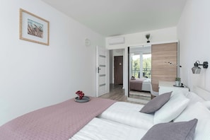 A modern bedroom with a bed, bedside table, and a mirror. - Air Conditioned Apartment with Balcony | Parking (Mielno)