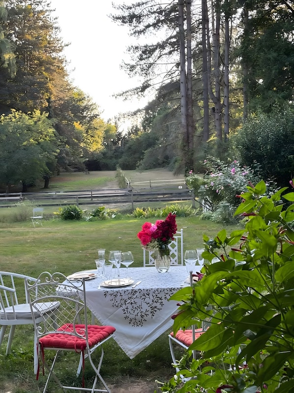 An outdoor dining area with a table set for four, surrounded by chairs with red cushions, a white tablecloth, and a vase of flowers.