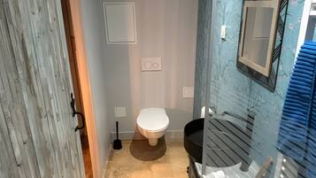 Et badeværelse med toilet, bidet, vask og et spejl på væggen.