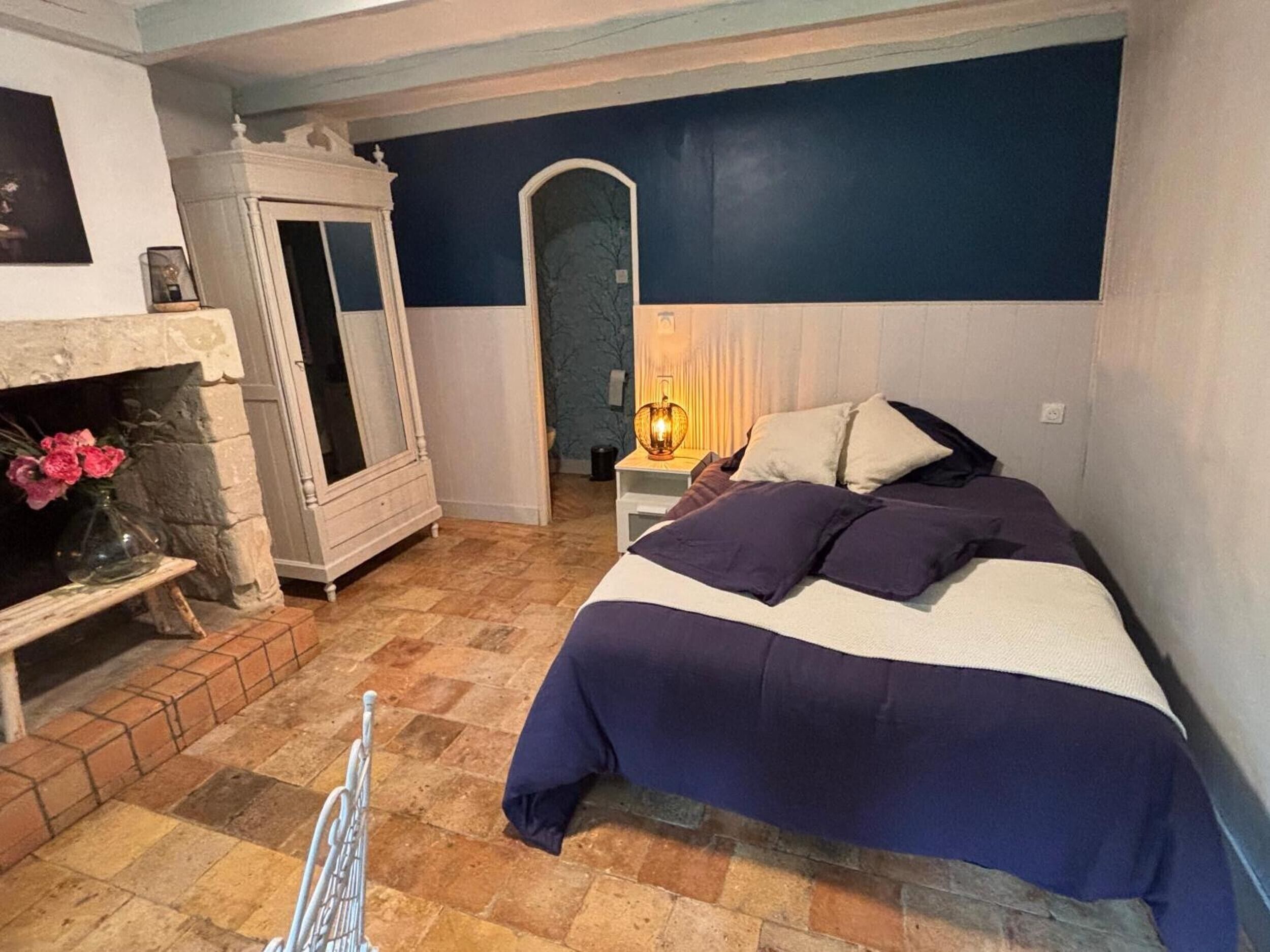 A bedroom with a bed, a fireplace, a nightstand, and a mirror.