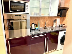 A compact kitchen with a microwave, oven, sink, and a washing machine. - Schiller 14 :  3 Bedrooms Apart Munich City Center (München)