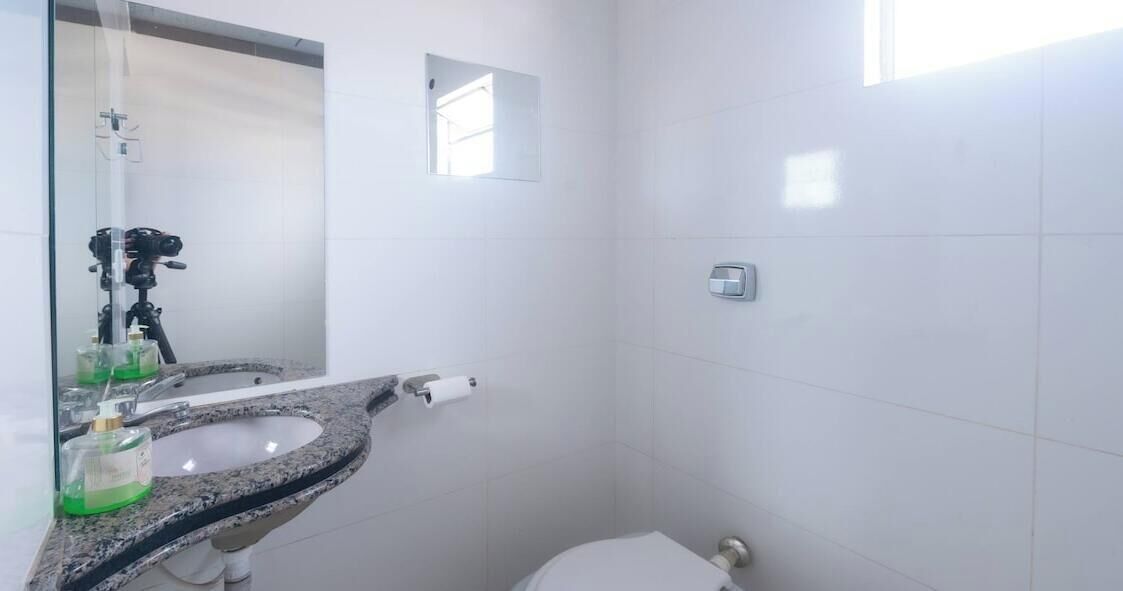 A bathroom with a granite countertop sink, a mirror, a toilet, and a small window.