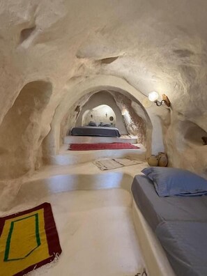 An underground room with a bed, a small table, and a lamp.
