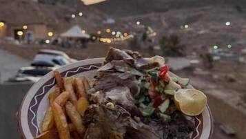 Una persona sostiene un plato con comida, un paisaje desértico y una puesta de sol al fondo.