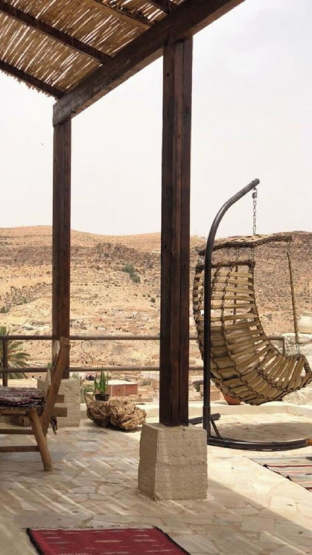 A wooden structure with a hanging chair and a table, overlooking a desert landscape.