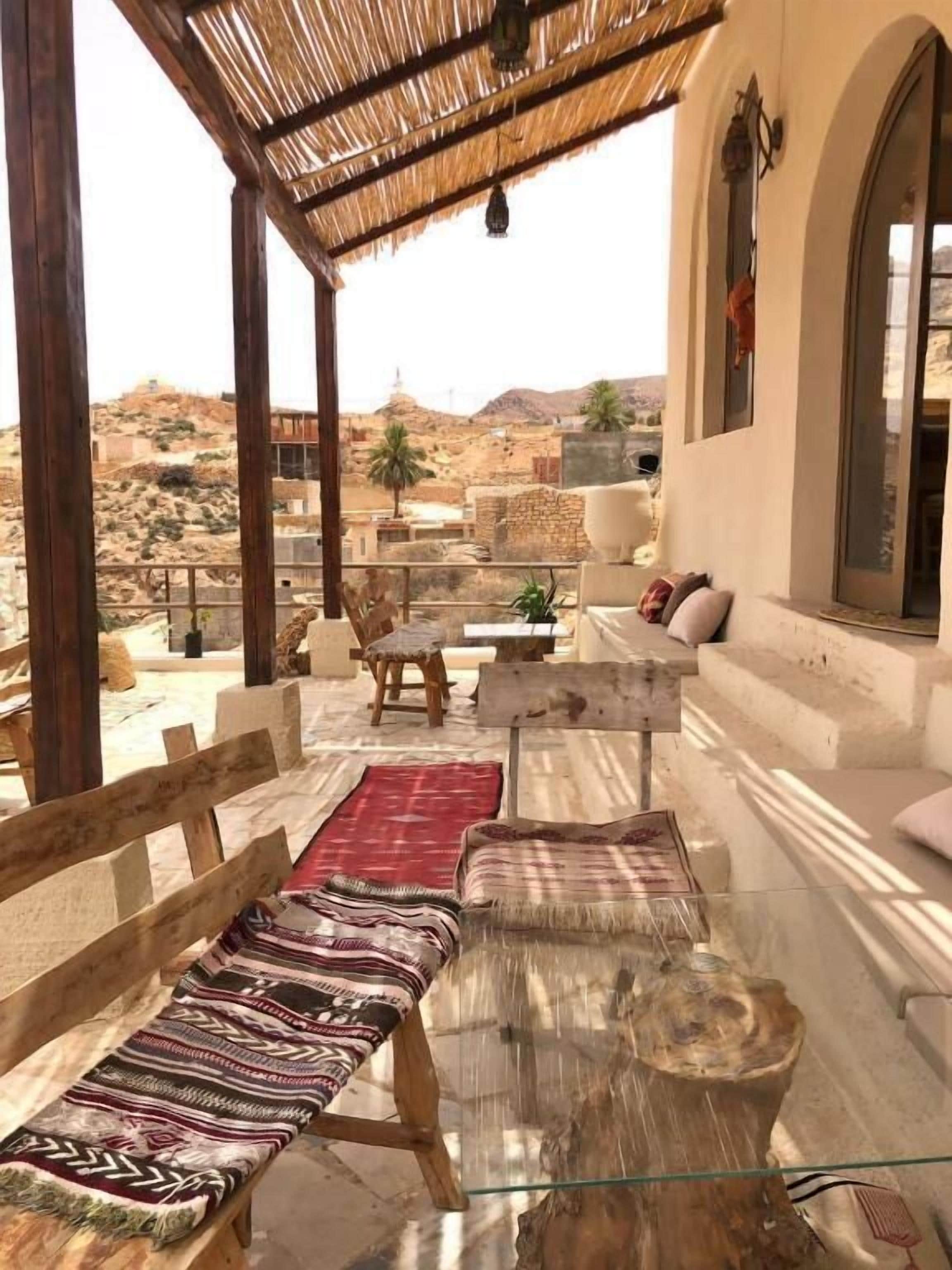 A covered outdoor seating area with benches and a table, overlooking a desert landscape.