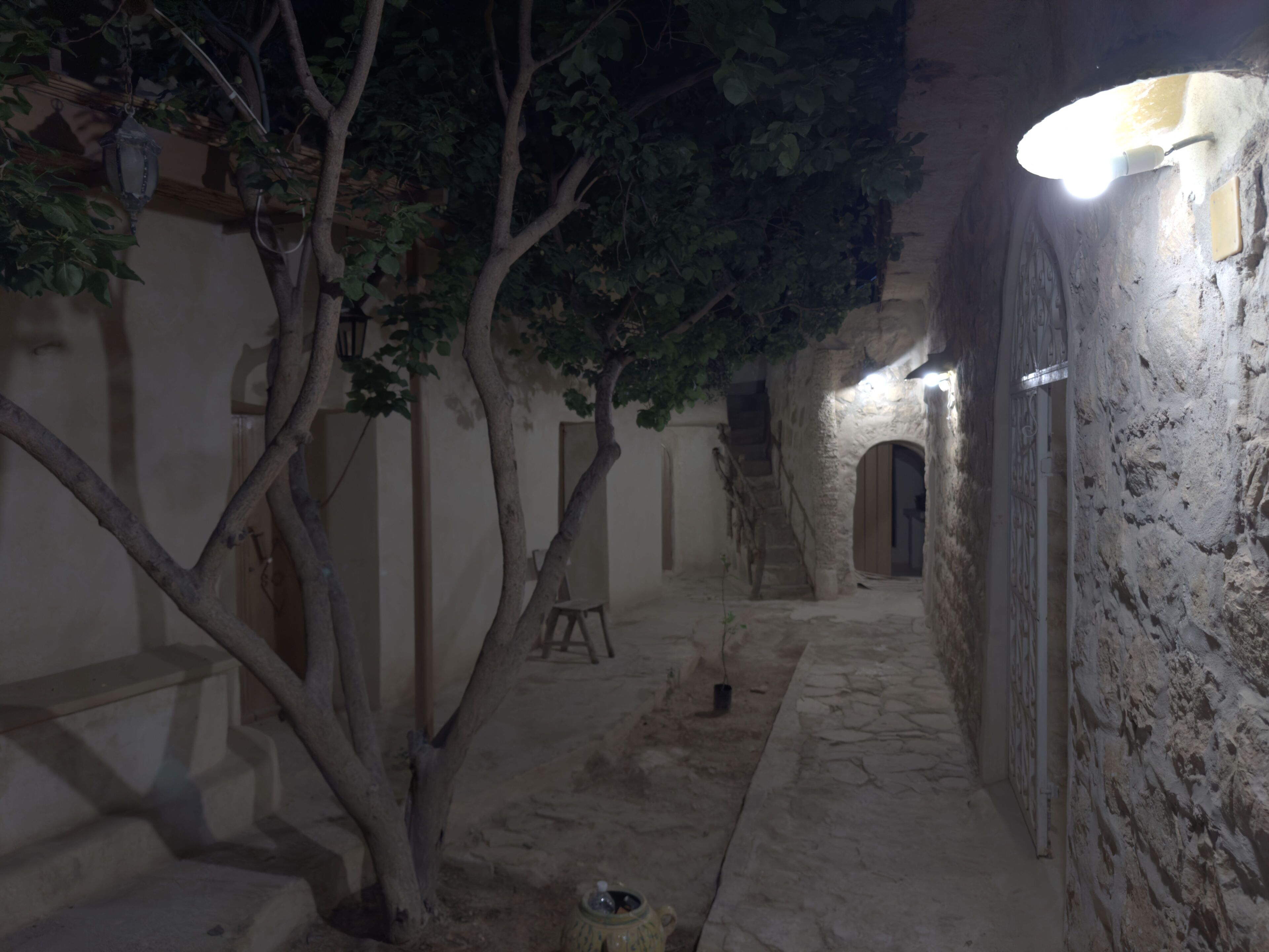 A narrow stone pathway leading to a wooden door, surrounded by walls with a rustic appearance.