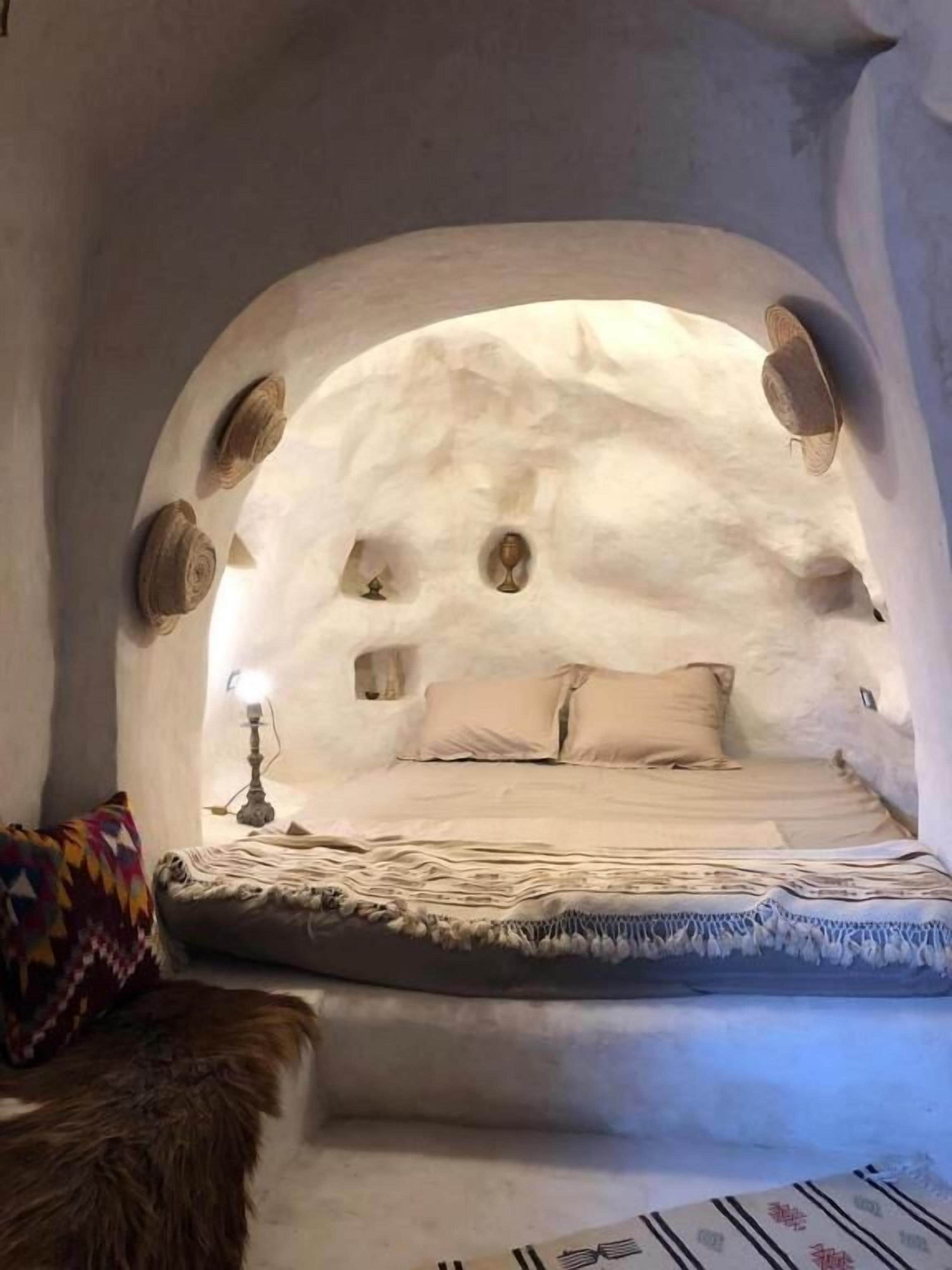 Een knus slaapkamer met bogen, een bed, kussens en een lamp.