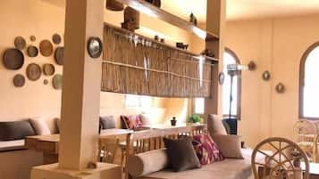 Una sala acogedora con un sofá, una silla de madera y una mesa de comedor. Se observan estanterías con objetos decorativos y un ventanal grande.